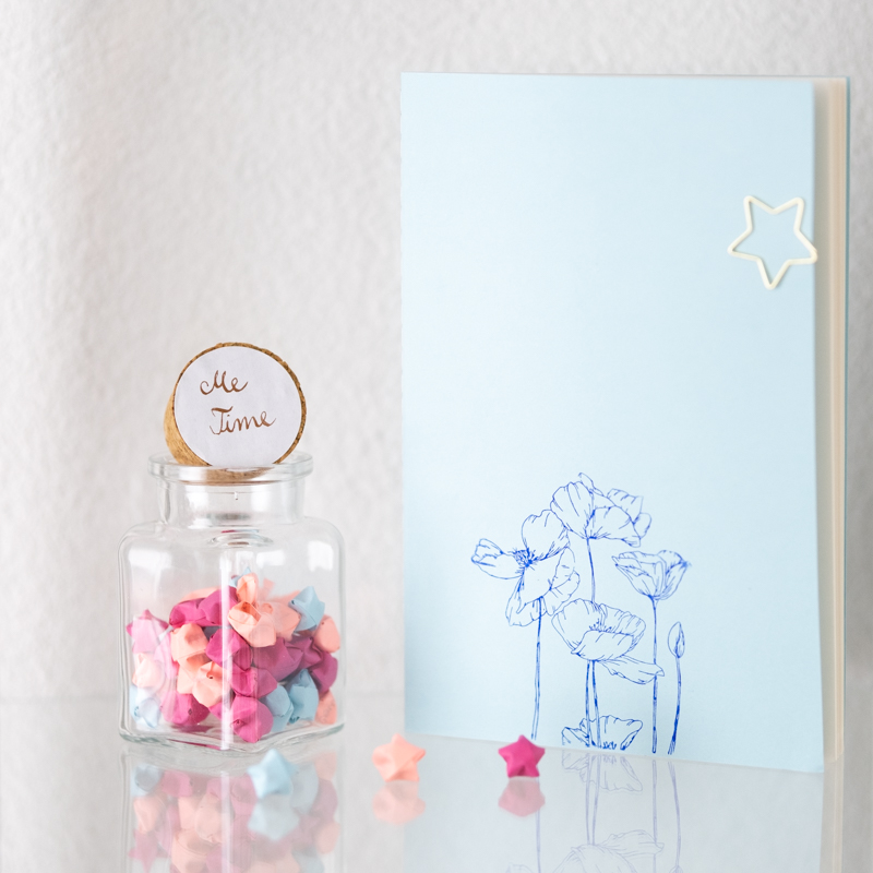 The Science Behind My Quests: Neurodivergent Productivity Tools Through Narrative Framing. photo of a blue botebook with flowers on the cover and a glass jar with colorful origami stars inside